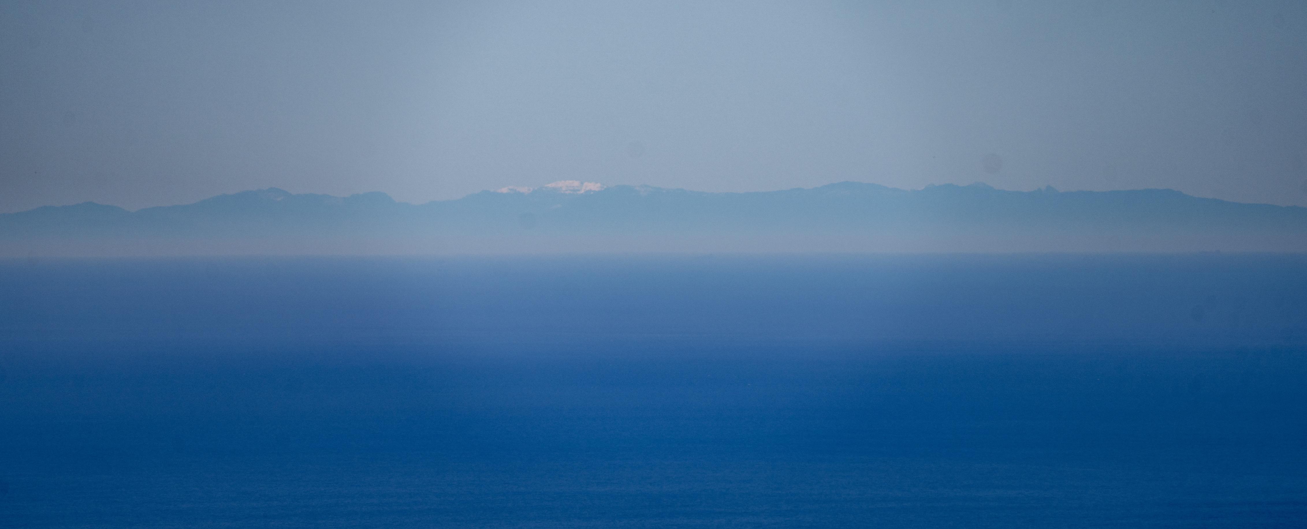 The blue Mediterranean sea and behind that coming out of the haze are the Riff mountains in Morocco, Africa. You can see snow on one of the mountains.