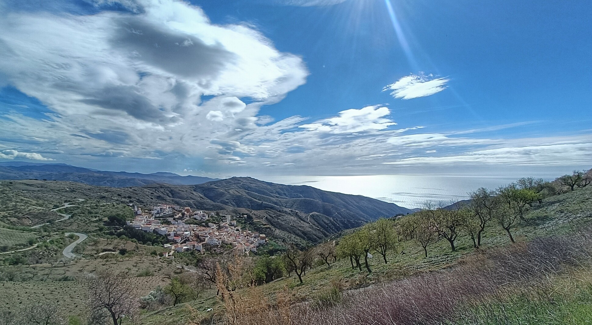 Looking over an almond grove down on a Spanish hillside village, sun shining on the Mediterranean sea and the sky full of forming lenticular clouds