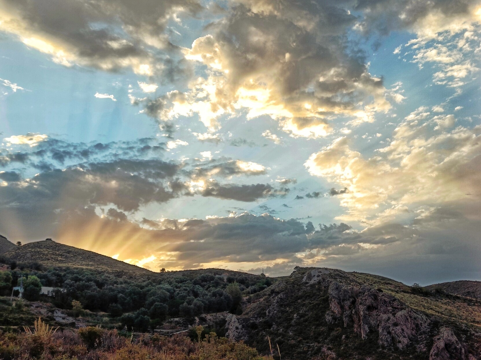 The sun rising behind the hills with its rays bouncing through some cloud