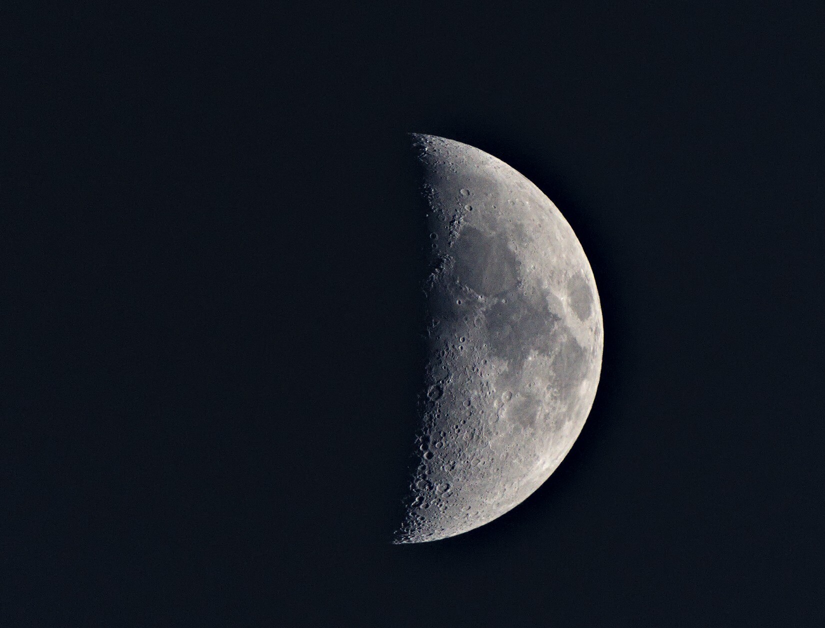 A photo of a half moon seeing clearly the craters and other markings on the moon. 