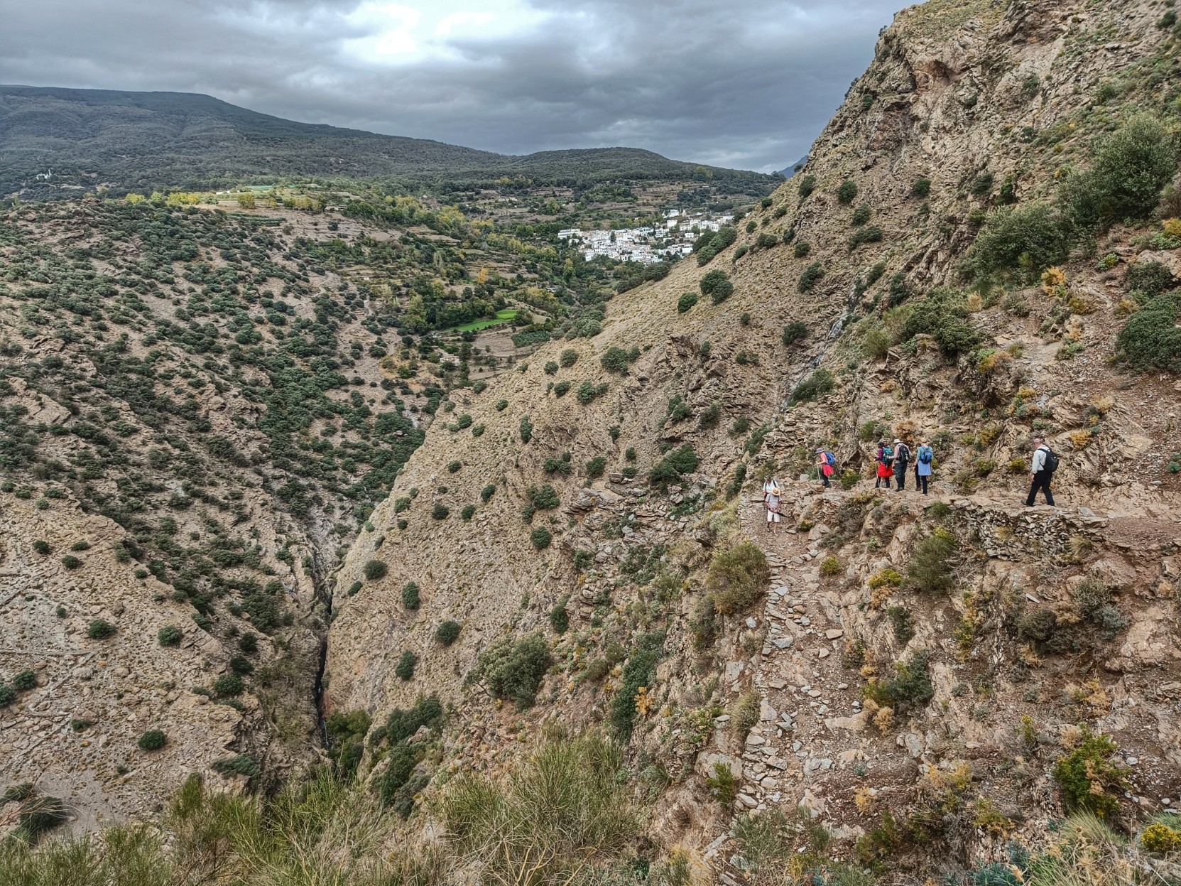 The village of Busquistar on the hillside with a group of walkers making their way down the gorge to cross the Rio Trevelez