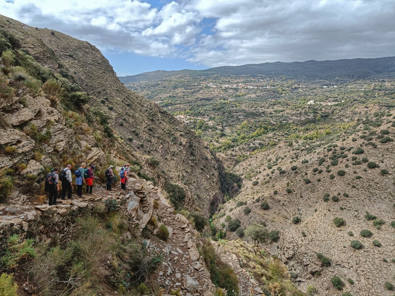 A group of walkers heading down into the Trevelez valley following an old trade route. In the background on the opposite side of the valley are a few of the white villages of La Taha.